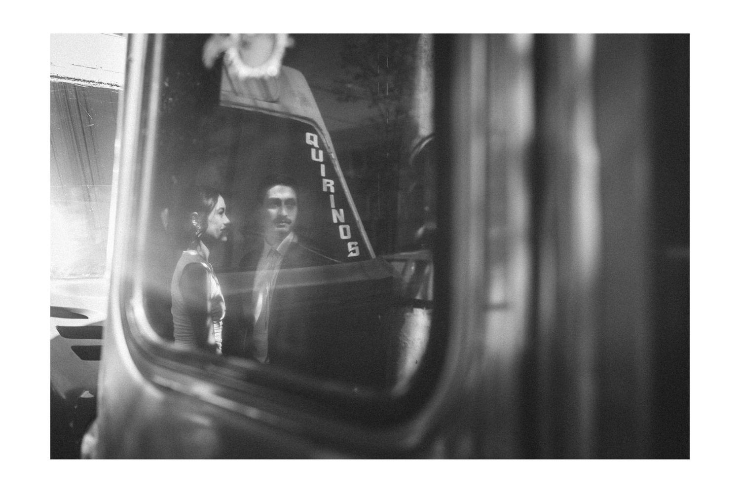 Black and white reflection in a car side mirror showing two people inside a vehicle.