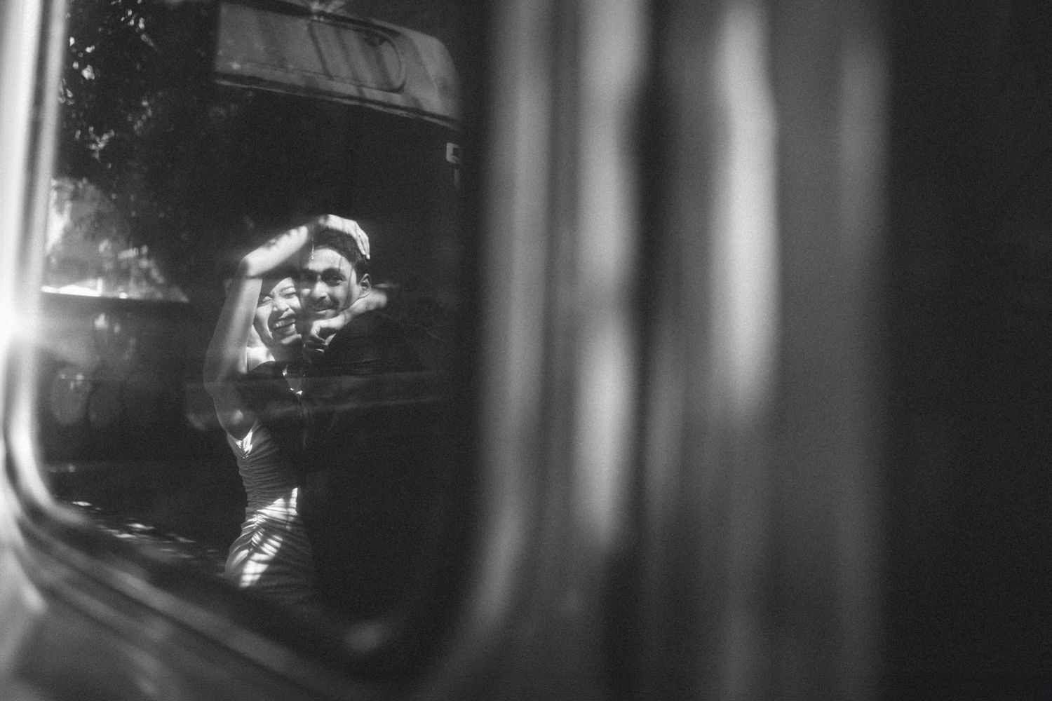 Black and white view through a train window showing passengers framed in reflective glass during travel.