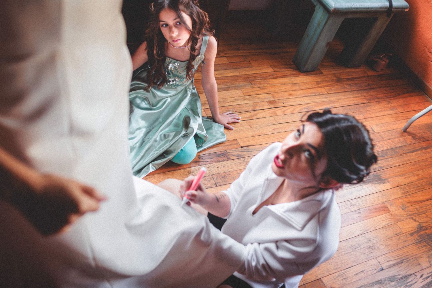 People laughing and sitting on hardwood floor during a casual indoor gathering.