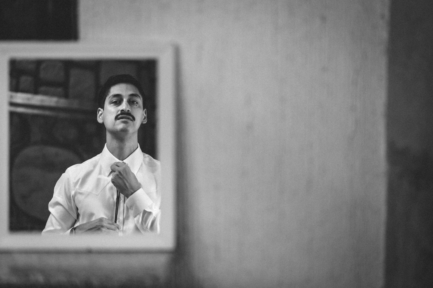 Black and white reflection in mirror shows person adjusting necktie while getting dressed.