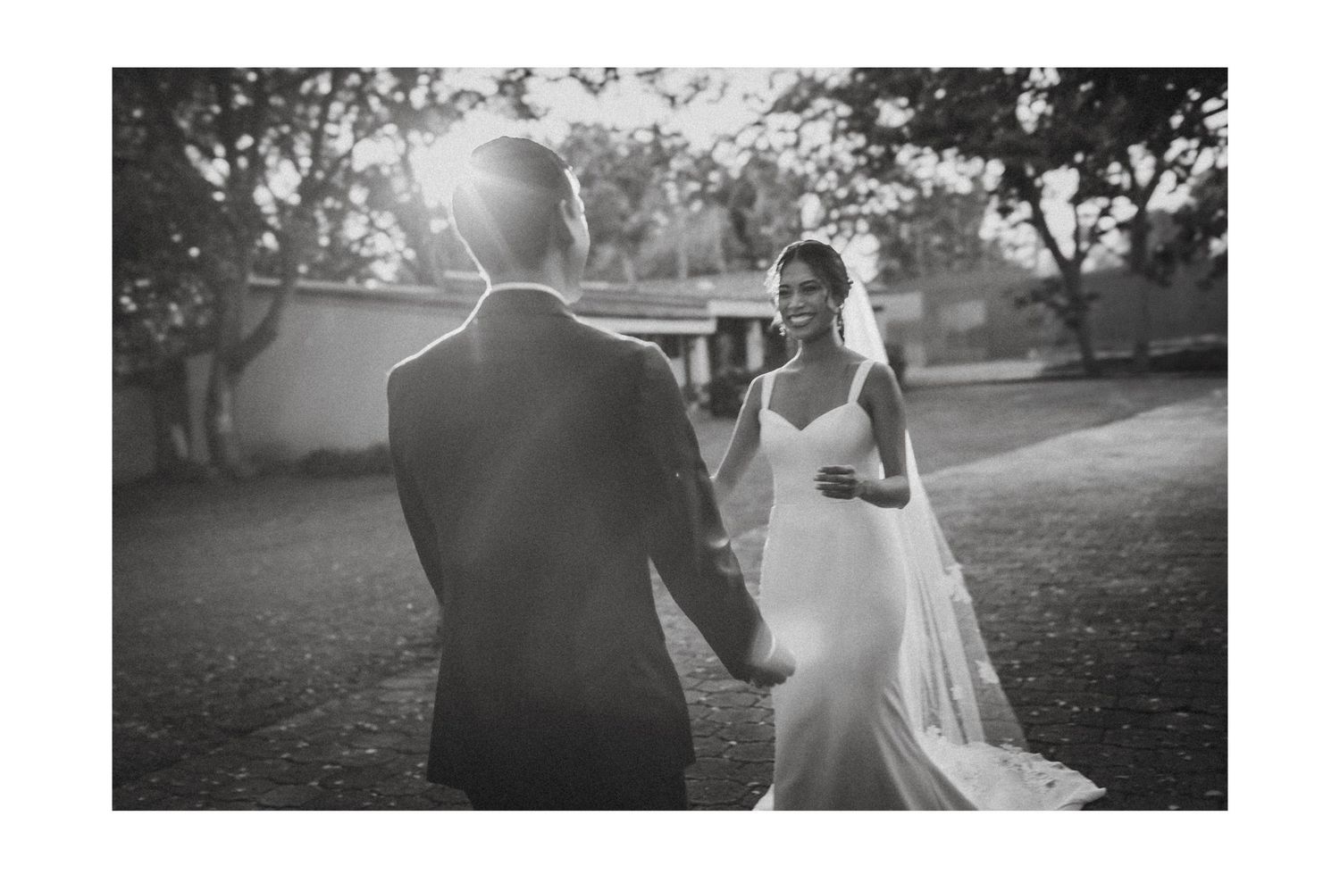 A black and white photo of a couple dancing outdoors during their wedding, with the bride wearing a flowing white dress.