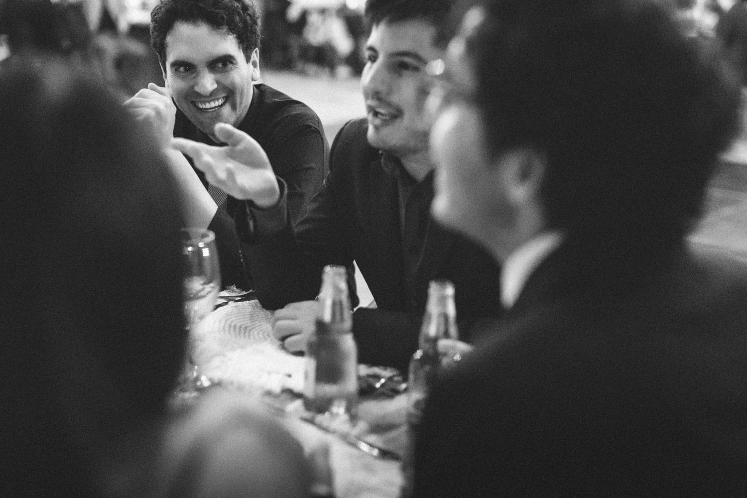 A black and white candid sequence of people gathered around a table enjoying a meal together at a social event.