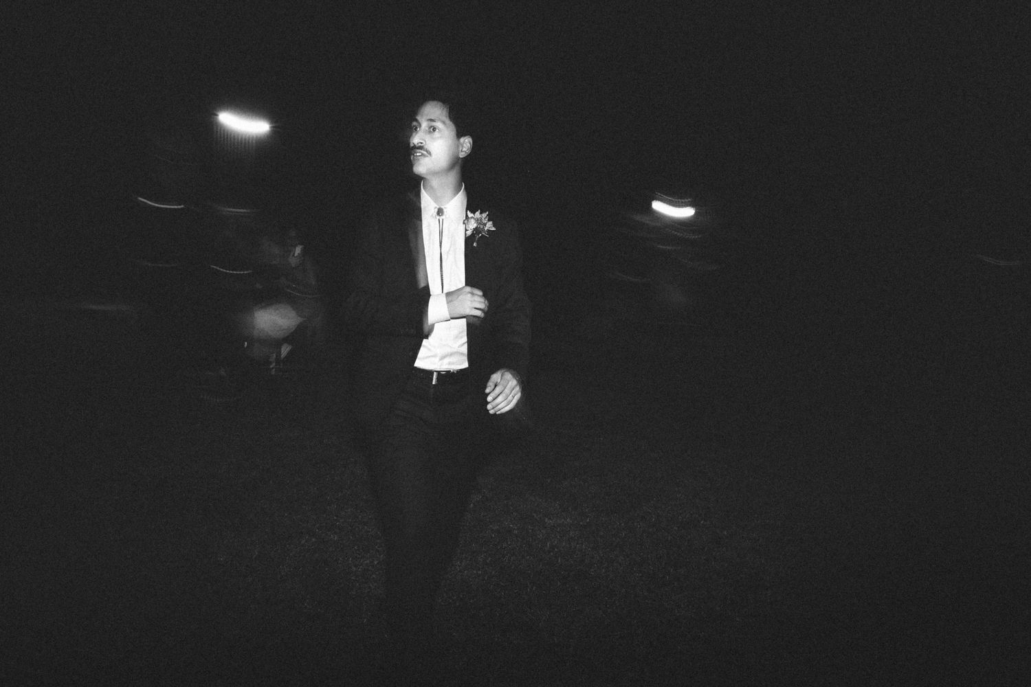 A performer in a black and white suit dances on a dark stage with spotlights illuminating their silhouette.