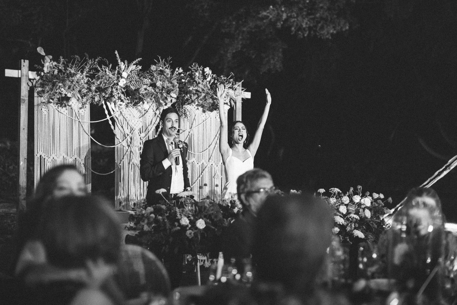 Group of guests dance and celebrate during an evening wedding reception under string lights and trees.