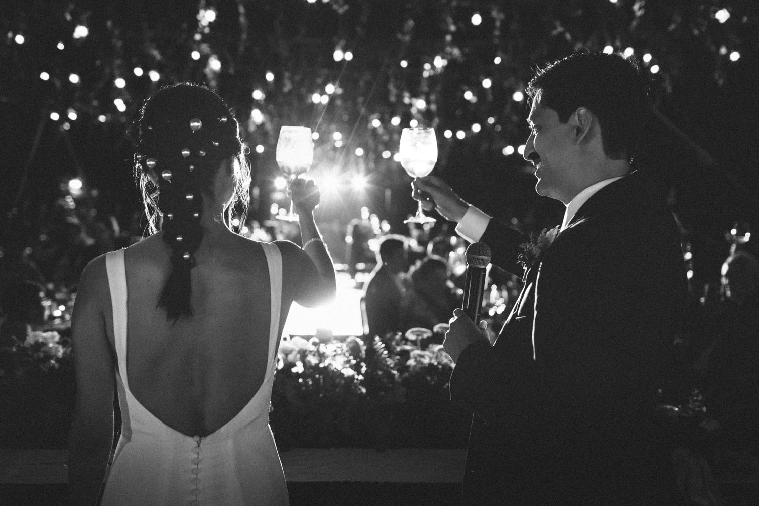 Black and white photo of a couple at an outdoor nighttime celebration with glowing lights and sparklers in the background.