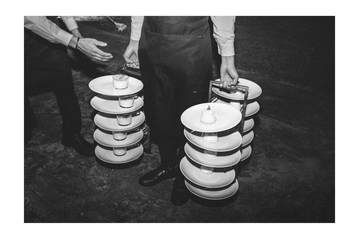 A black and white photograph shows hands holding stacks of plates in what appears to be a restaurant setting.