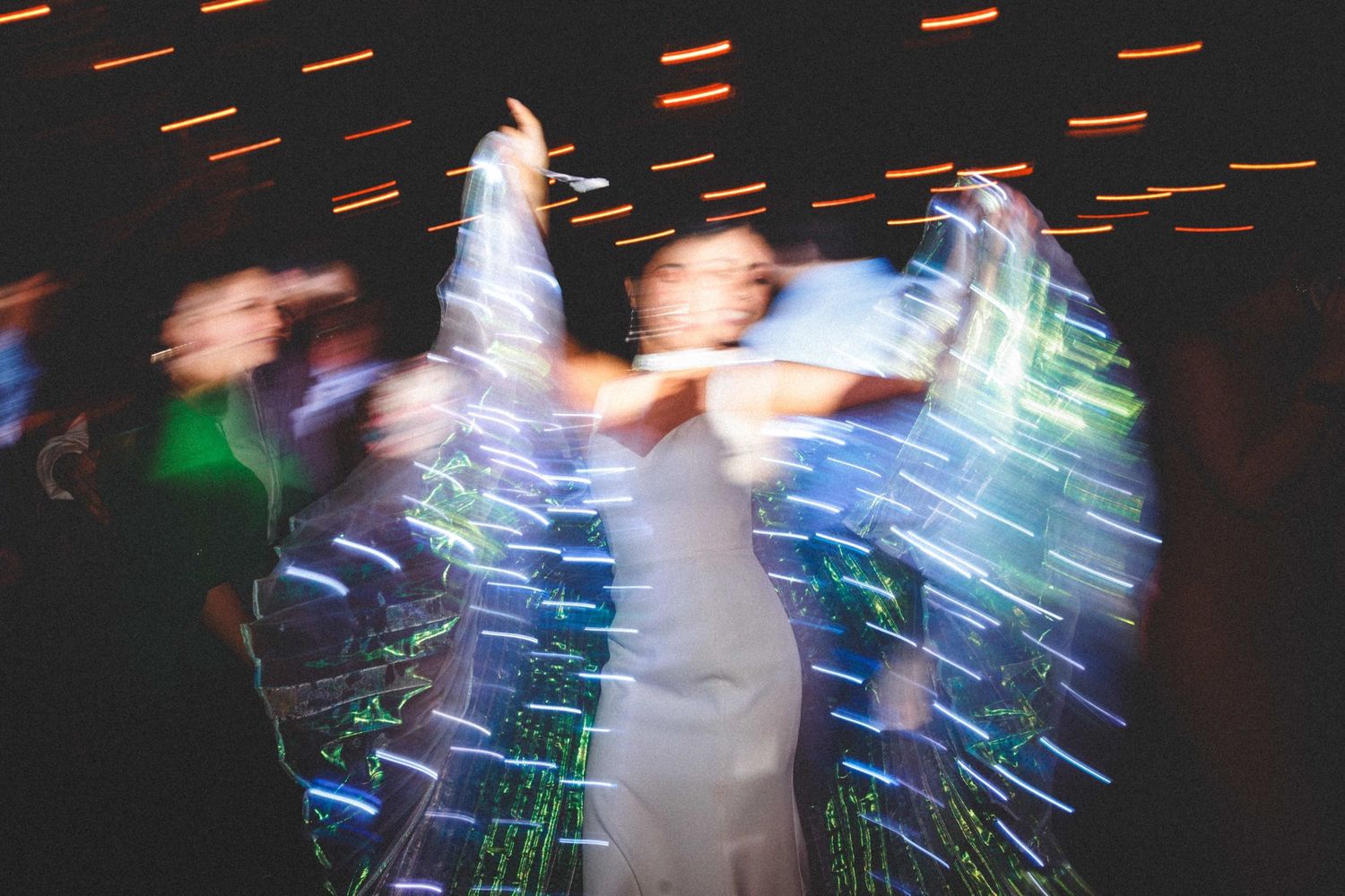 Long exposure photo of wedding dancers creating light trails and motion blur effects on a dark dance floor.