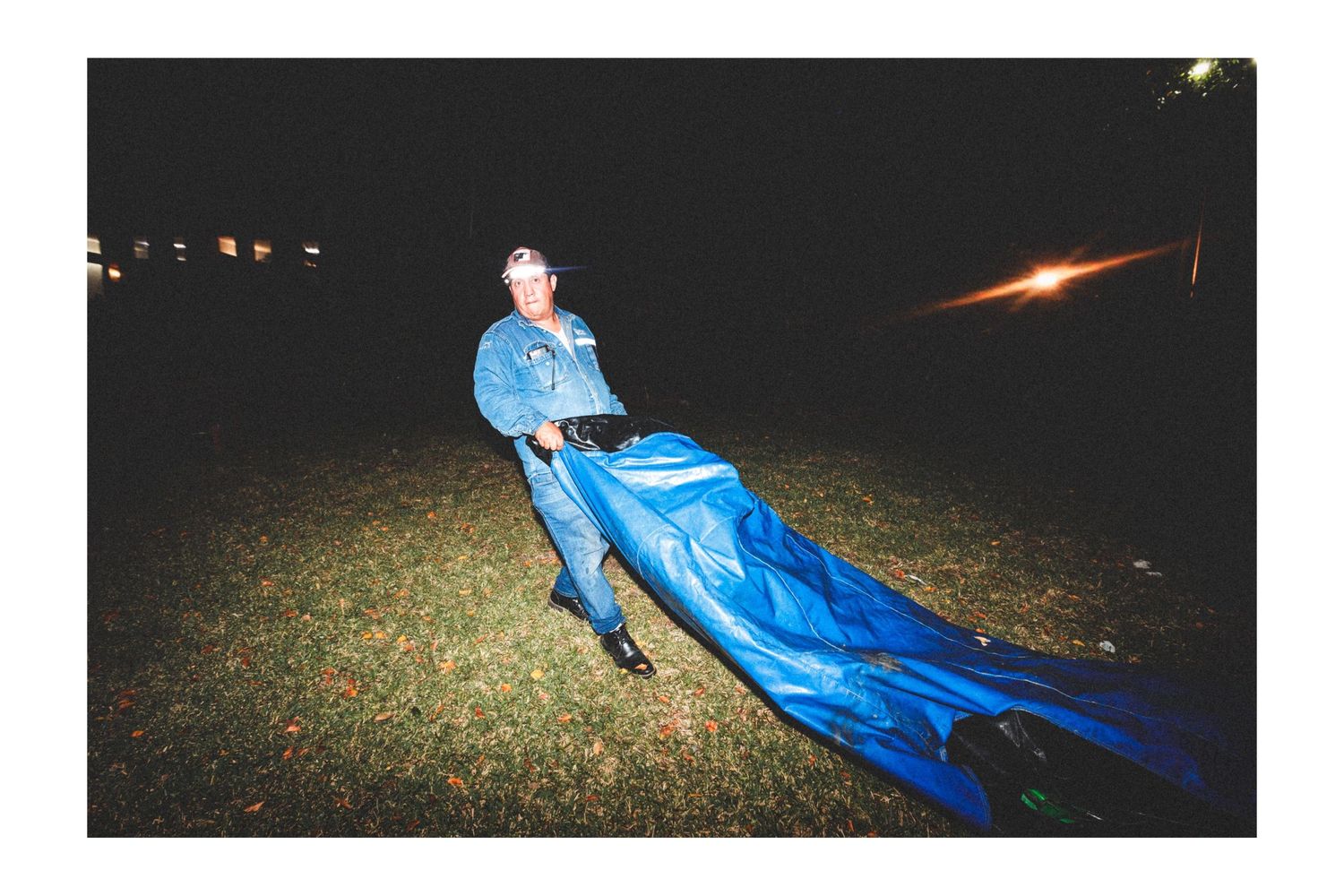 Someone in bright blue clothing drags a billowing fabric across dark grass at night.
