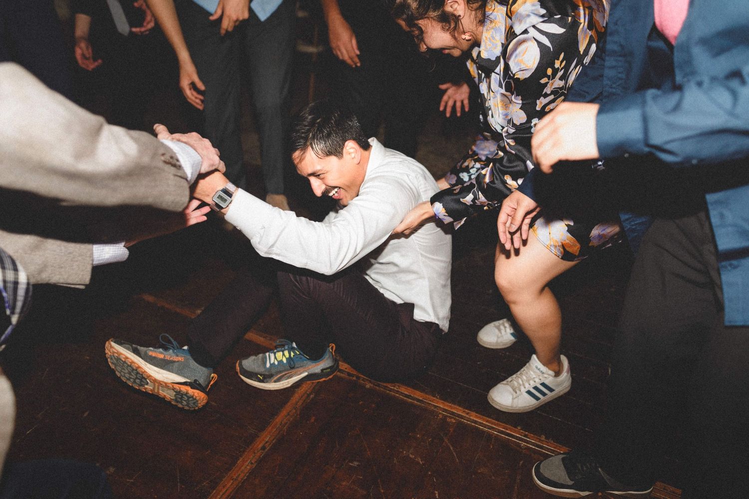 Close-up view of people's feet and legs on a dark wooden dance floor during a social dance gathering.