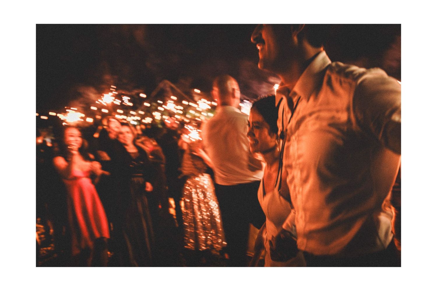People dance and celebrate at a nighttime gathering with warm lighting and orange tones creating an atmospheric scene.