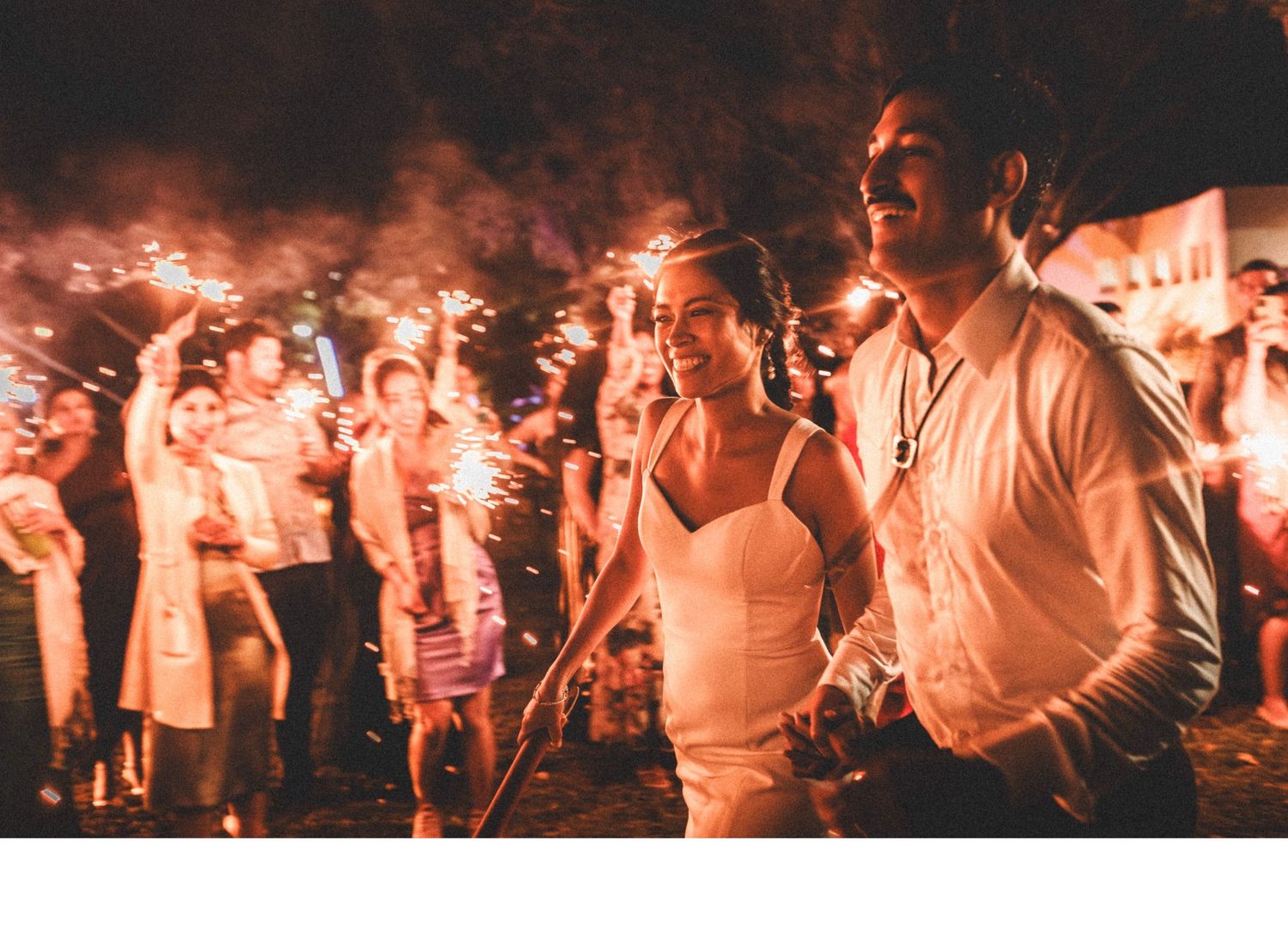 A couple dances together at a festive outdoor evening event with warm lighting and a crowd in the background.