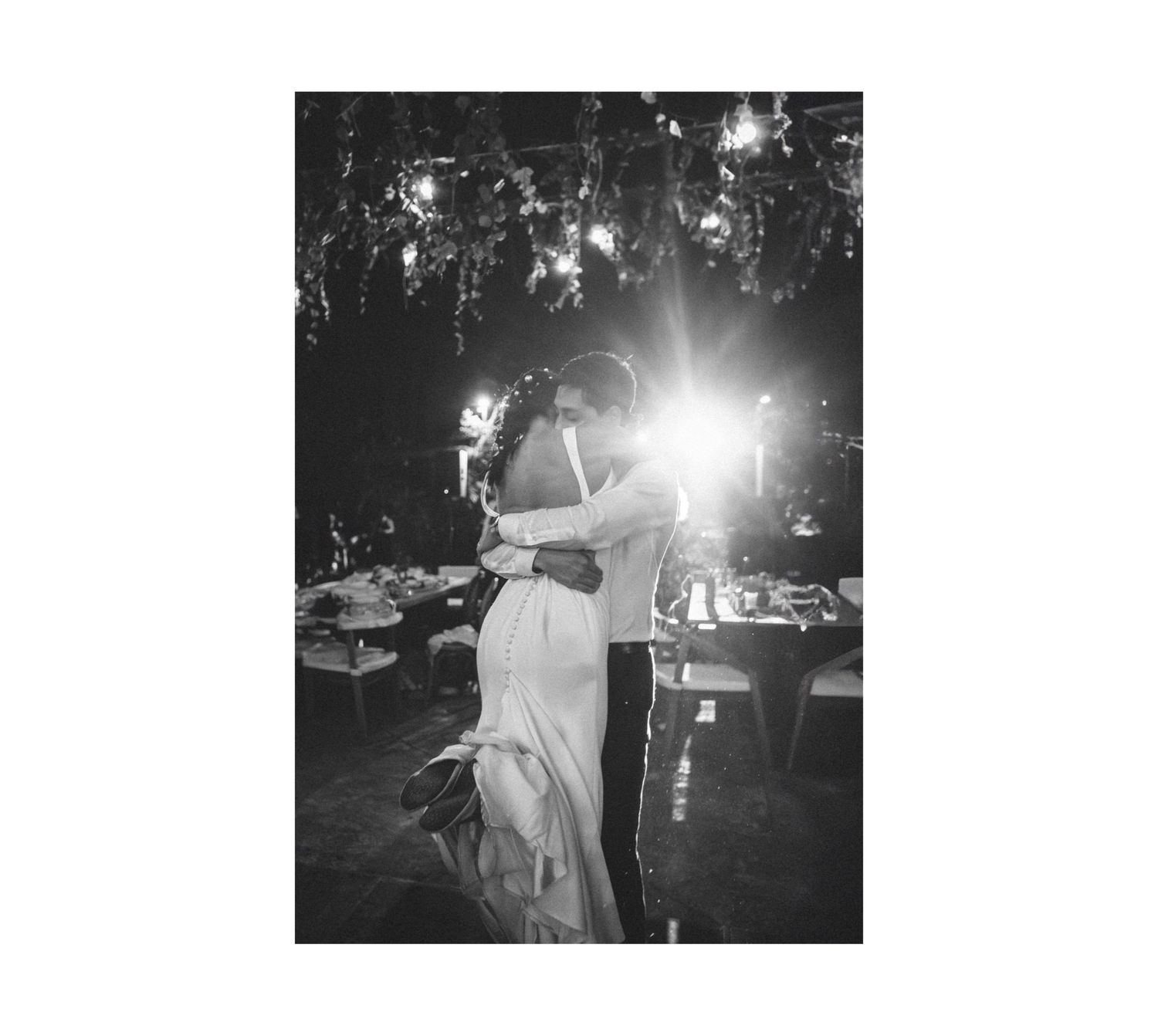 A couple dances together under dramatic lighting at an evening wedding reception in black and white.