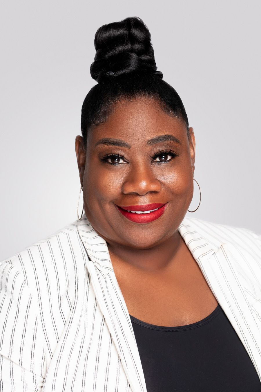 Professional portrait of woman in striped blazer and red lipstick against gray background.