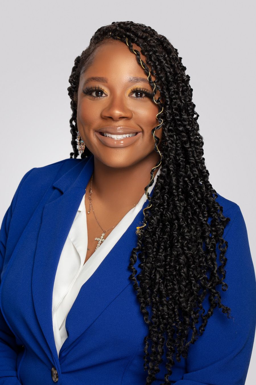 Professional headshot of woman in blue blazer with long braided hairstyle against gray backdrop.