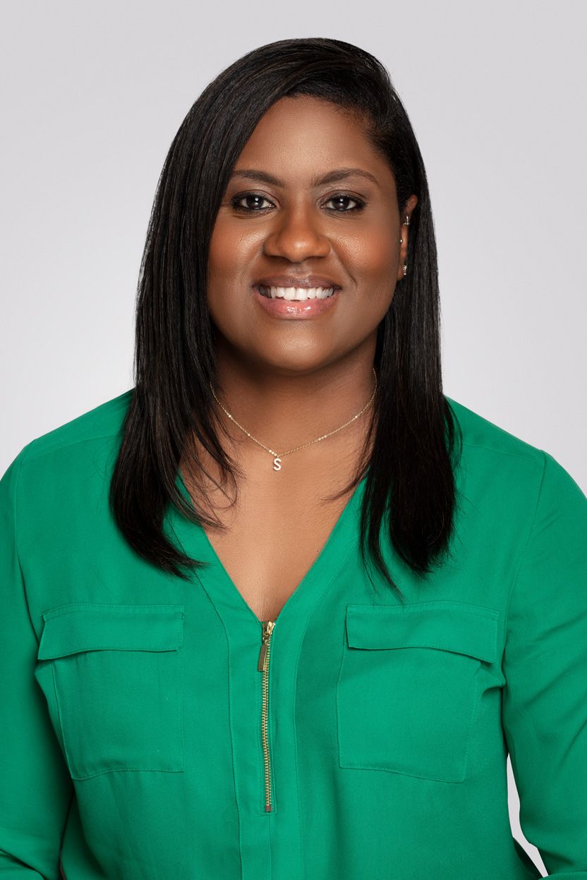 Professional portrait of woman in emerald green blouse with straight black hair against gray background.