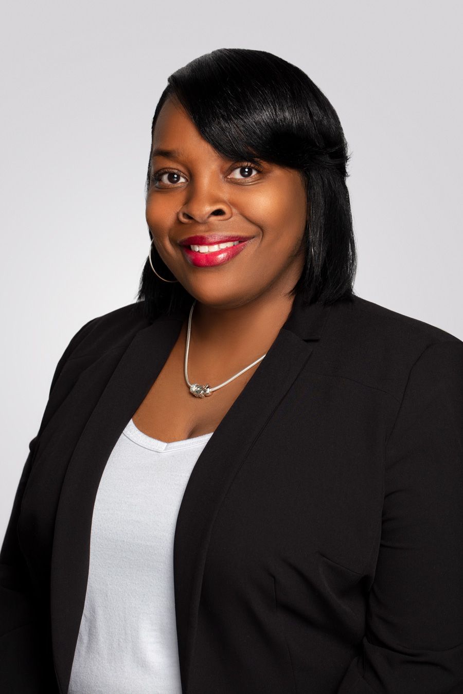 Professional portrait showing someone in a black blazer with a white top and silver necklace.