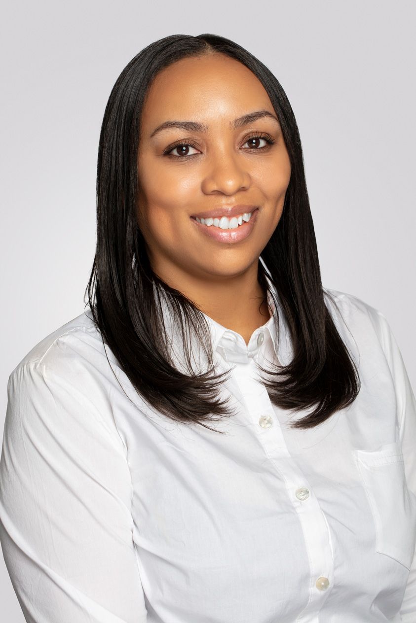 Professional headshot featuring someone in a white button-down shirt against a gray backdrop.
