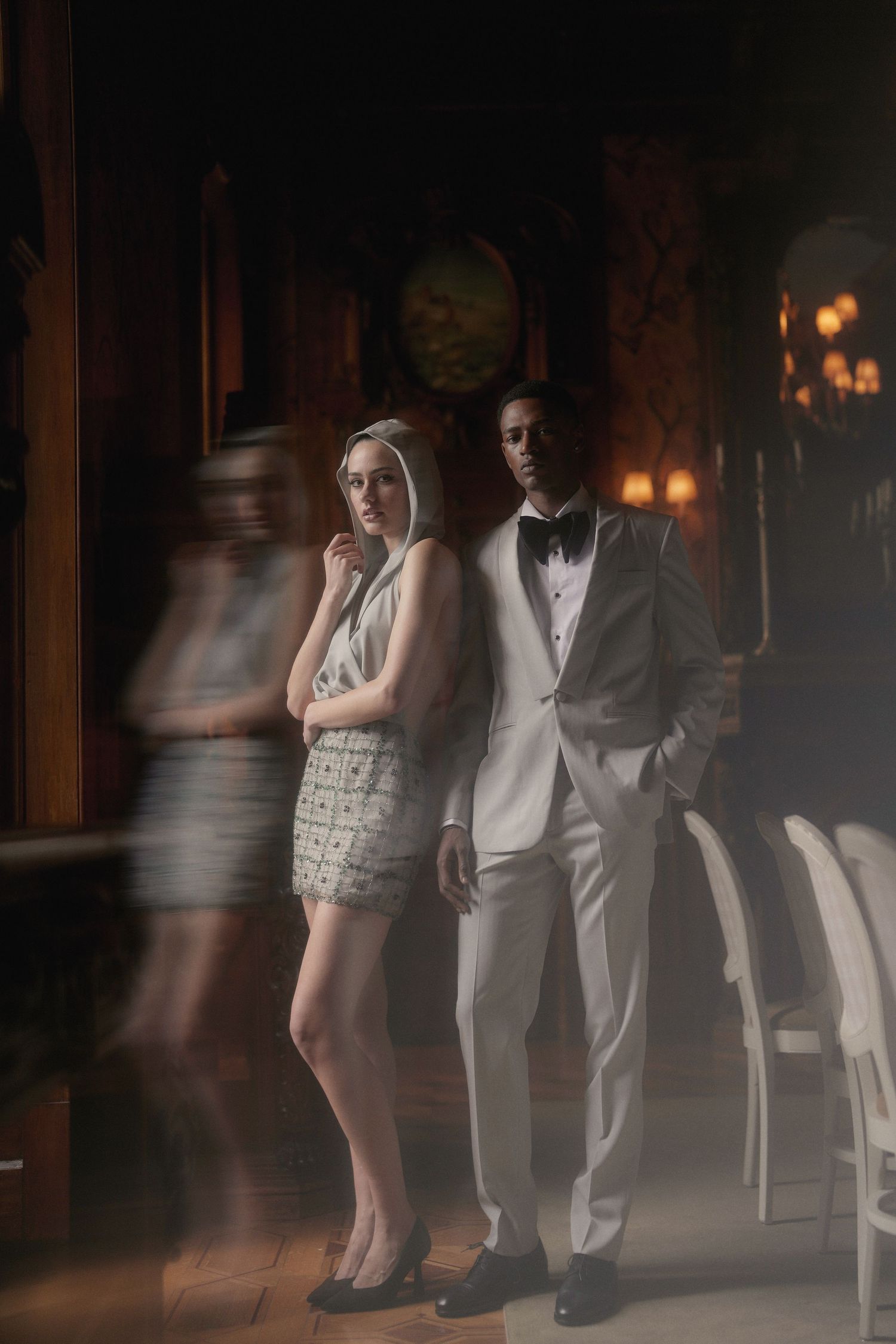 A couple in formal attire poses dramatically in a dimly lit venue with ambient lighting creating a moody atmosphere.
