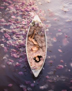 Dreamy portrait in a white boat surrounded by floating pink cherry blossoms on water.