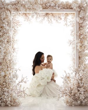 A tender moment captured in an ethereal setting with soft pink cherry blossoms framing a white dress against a bright background.