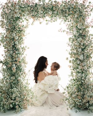 Intimate portrait under an elegant floral arch with baby's breath and white roses against light background.