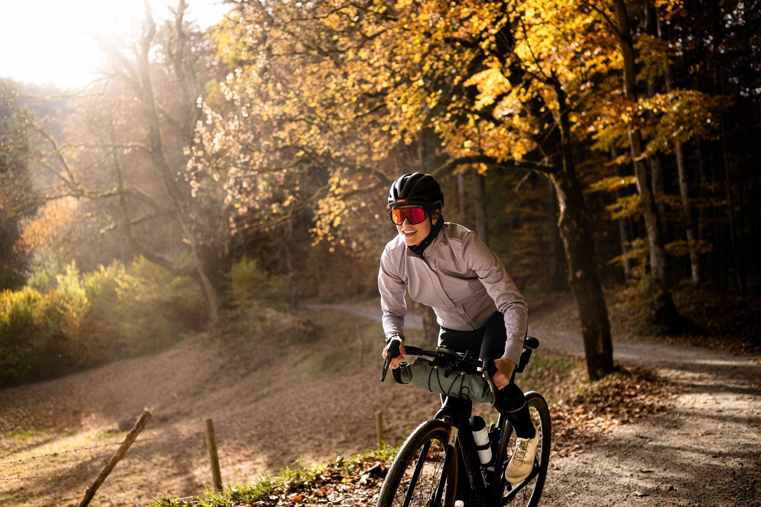 A cyclist rides through a scenic autumn forest trail with golden sunlight filtering through the trees.