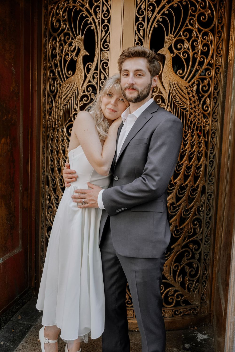 A bride and groom pose together against an ornate vintage door with intricate metalwork patterns.