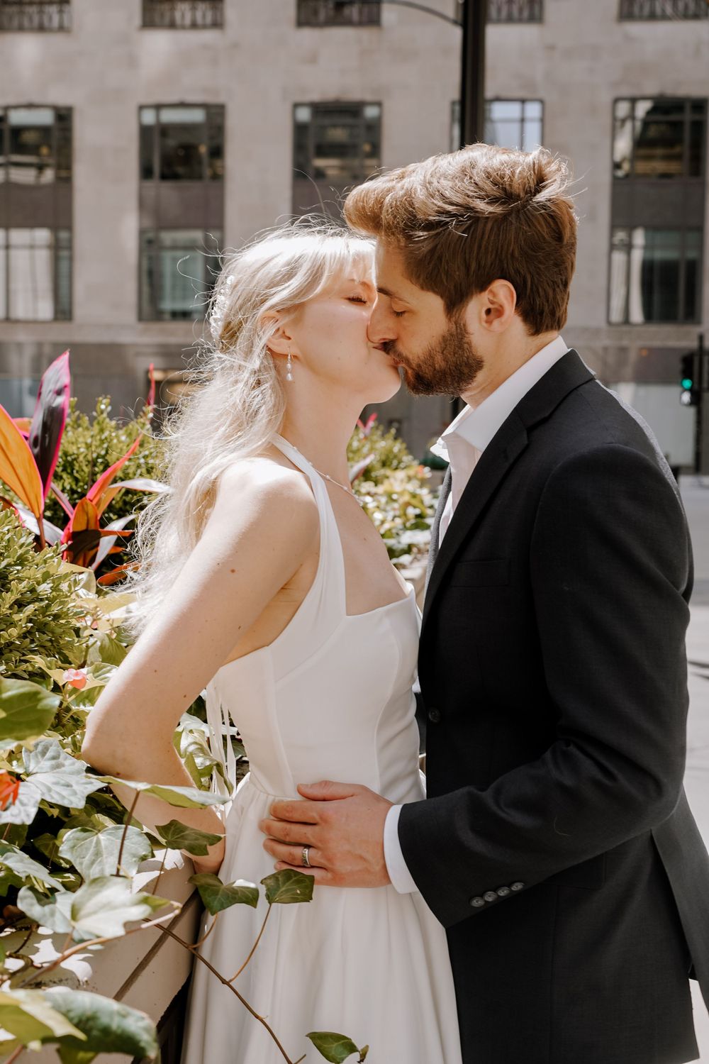 Romantic outdoor wedding scene with couple sharing embraces and kisses surrounded by greenery and sunlight.