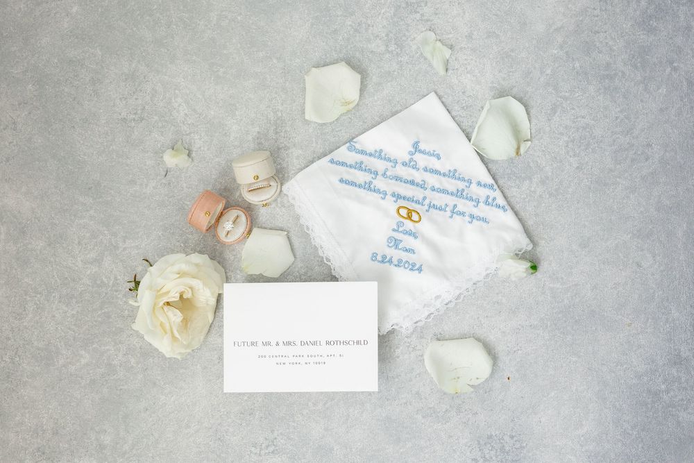 Wedding invitation and flower petals arranged on light gray textured surface with delicate white rose blooms.