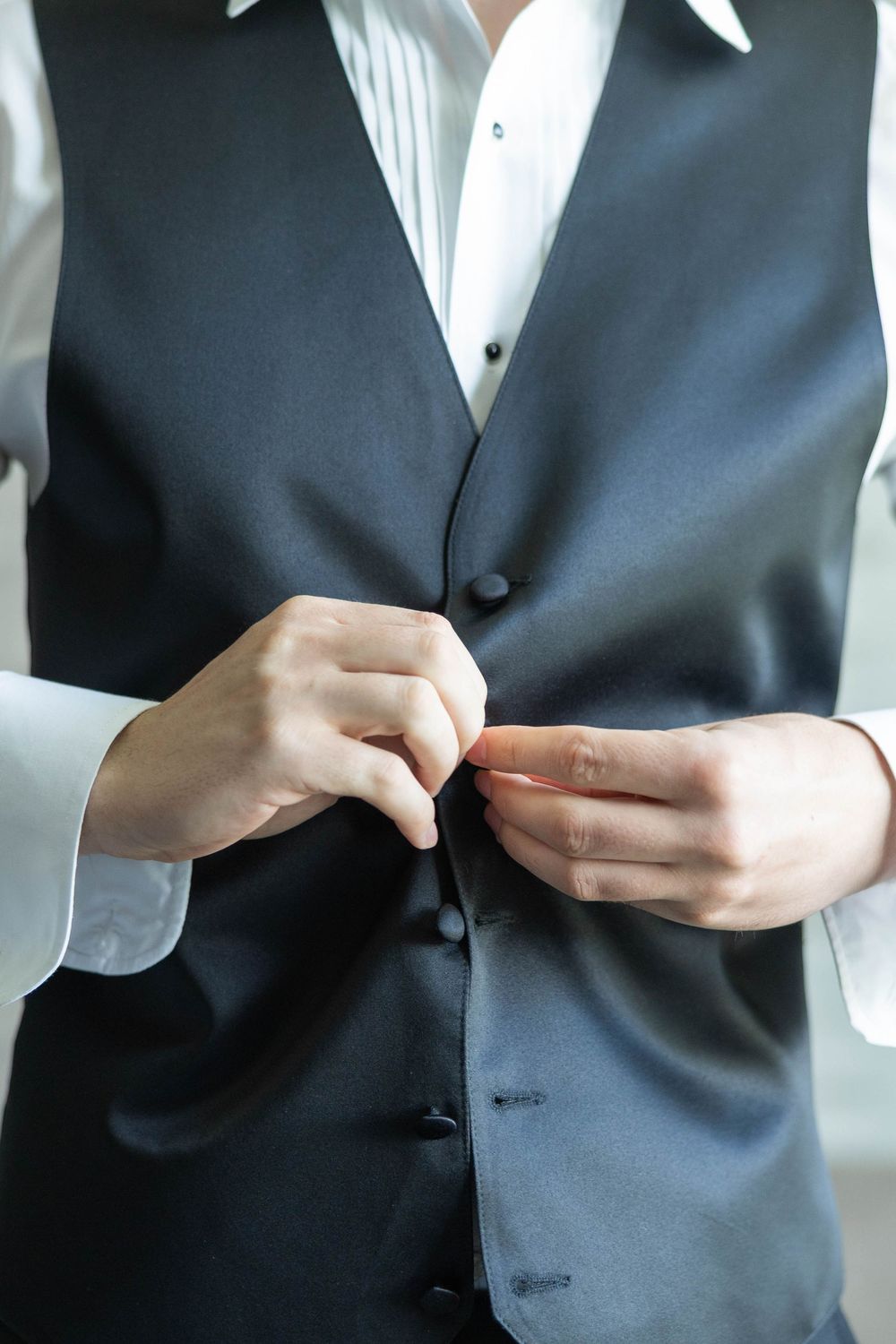 A person wearing a formal black suit vest buttons up their formal attire in a sequence of closeup shots.