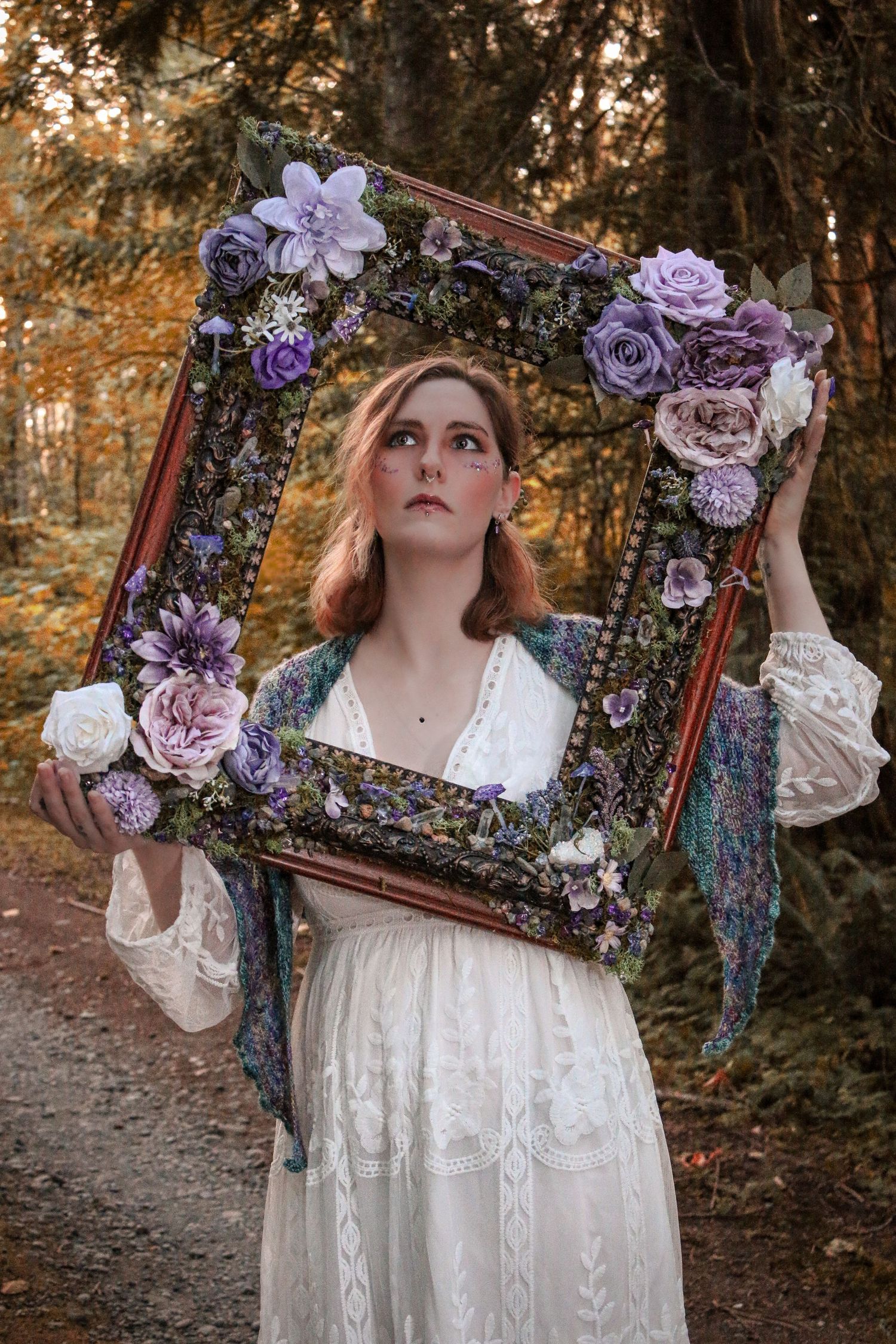 A vintage floral frame decorated with purple and pink roses held up in a dreamy autumn forest setting.
