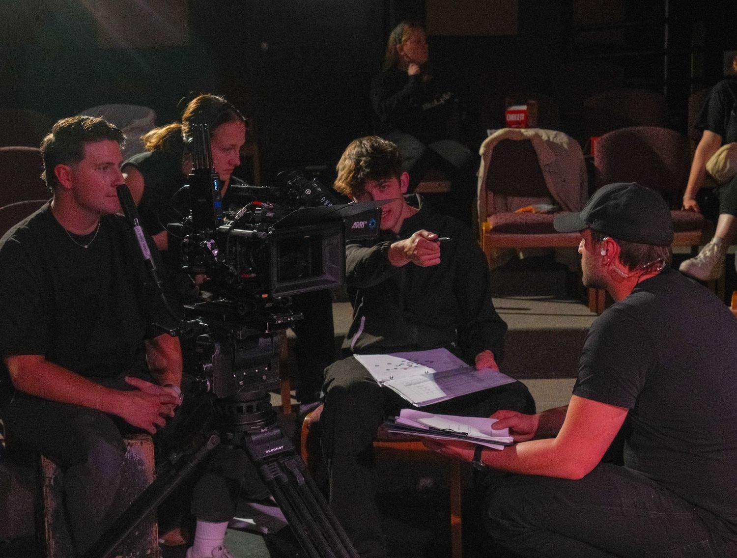 Film crew collaborating around a professional cinema camera during an indoor production shoot.