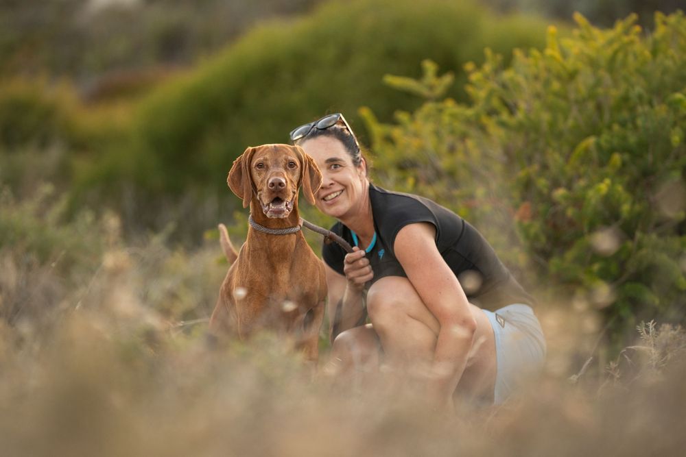 A brown Vizsla dog and companion pose together in the dunes at a Perth beach during sunset.