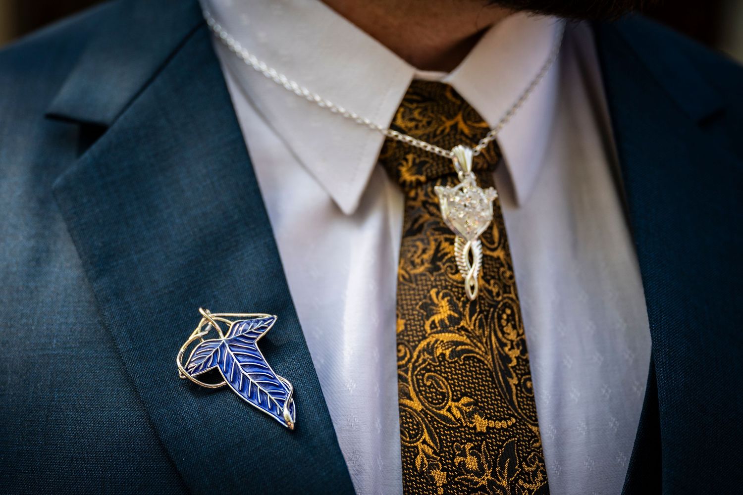 Close-up detail of blue suit jacket with ornate gold paisley necktie and small Charlotte Hornets team pin on lapel.