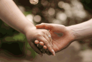 Two hands tenderly reaching for each other with a blurred green and bokeh background.