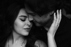 Black and white romantic couple portrait, woman smiling with eyes closed as man leans in close, engagement ring visible.