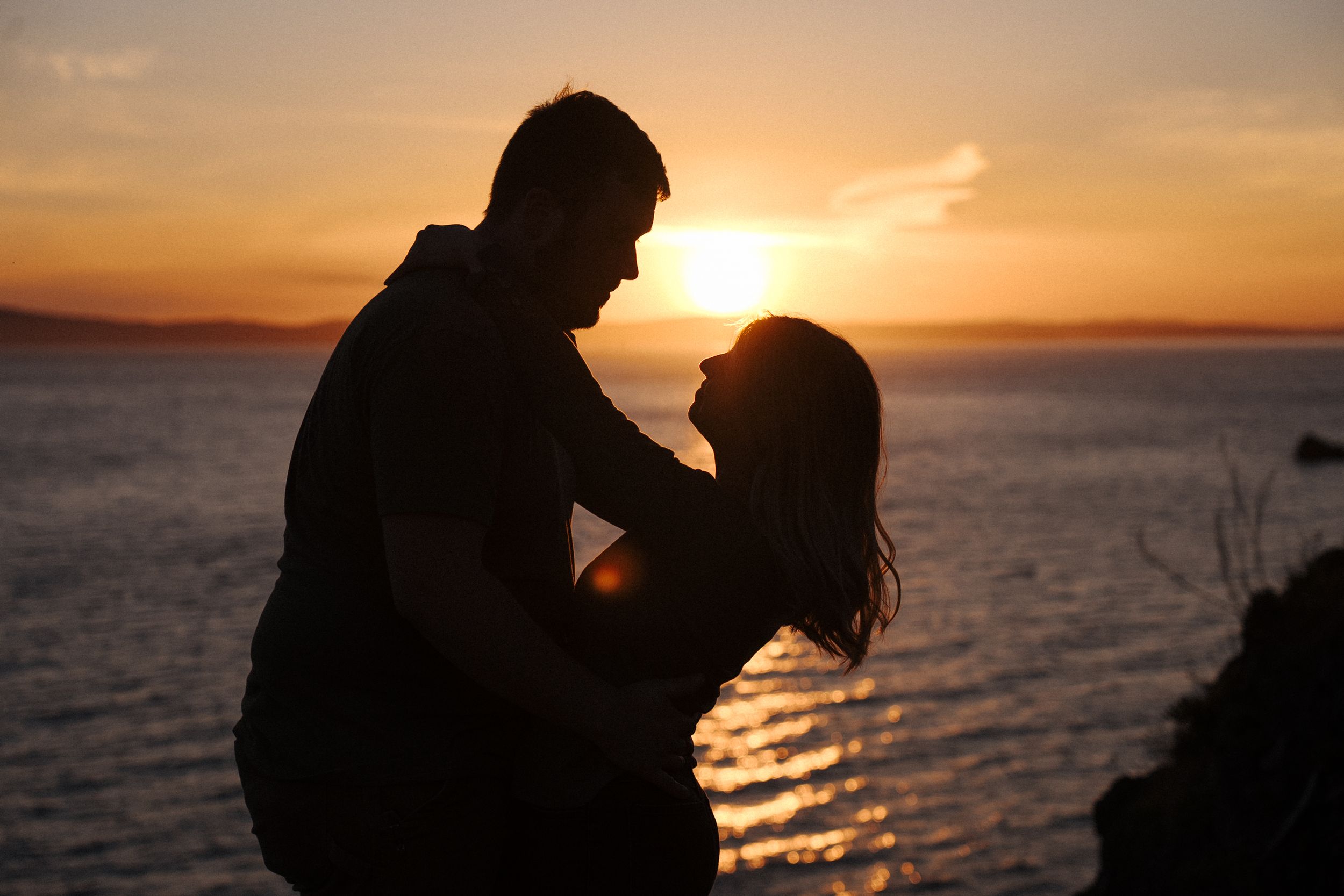 Four silhouettes of romantic couples against a dramatic sunset over the ocean.