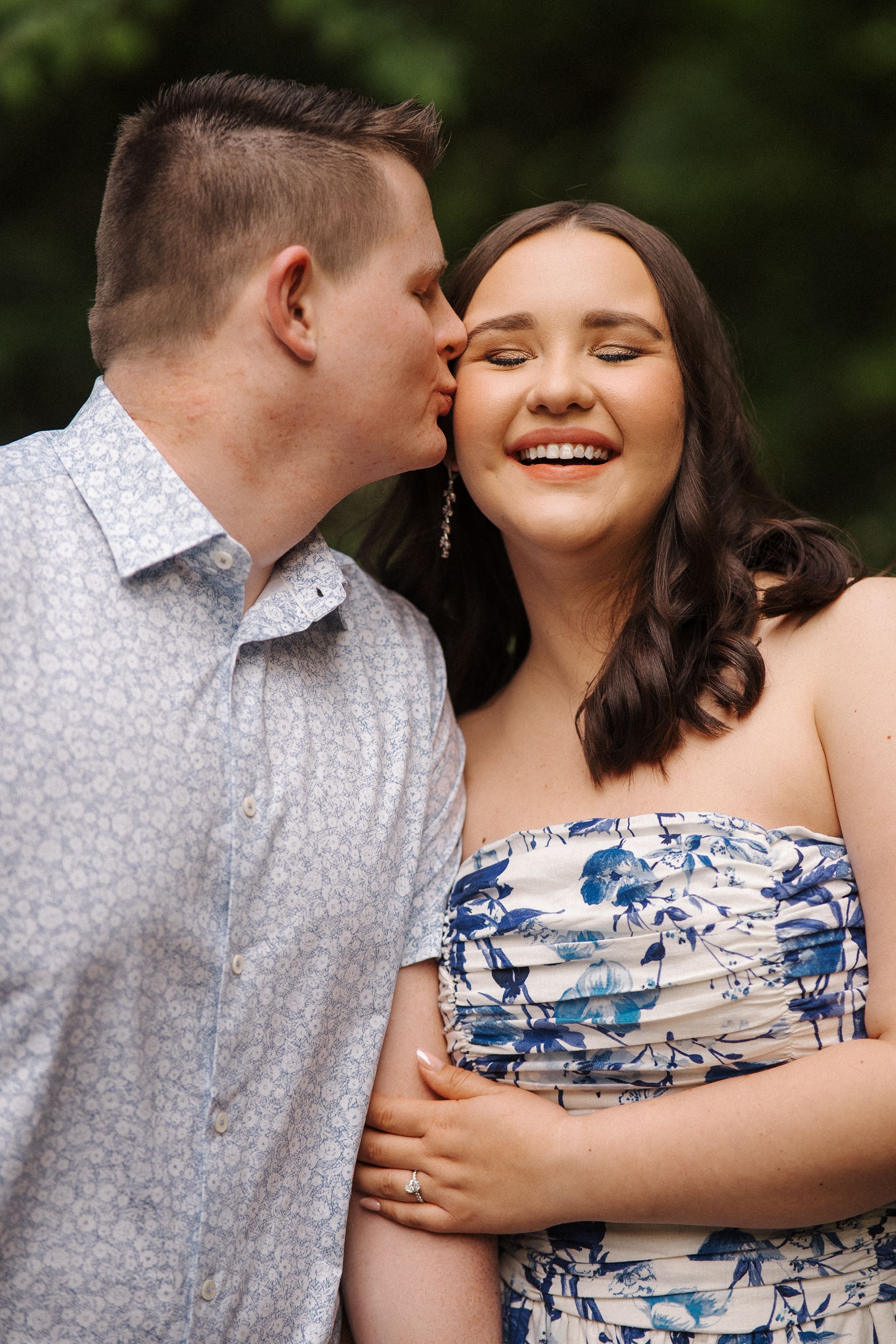 A couple shares a sweet moment outdoors, with one person wearing a patterned shirt and the other in a floral dress.