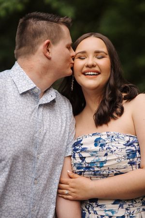 A couple shares a sweet moment outdoors, with one person wearing a patterned shirt and the other in a floral dress.