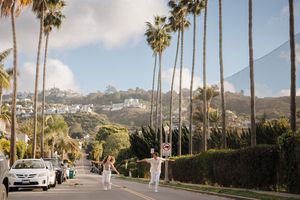Palm tree-lined residential street in Southern California with mountains in background and parked car on sunny day.