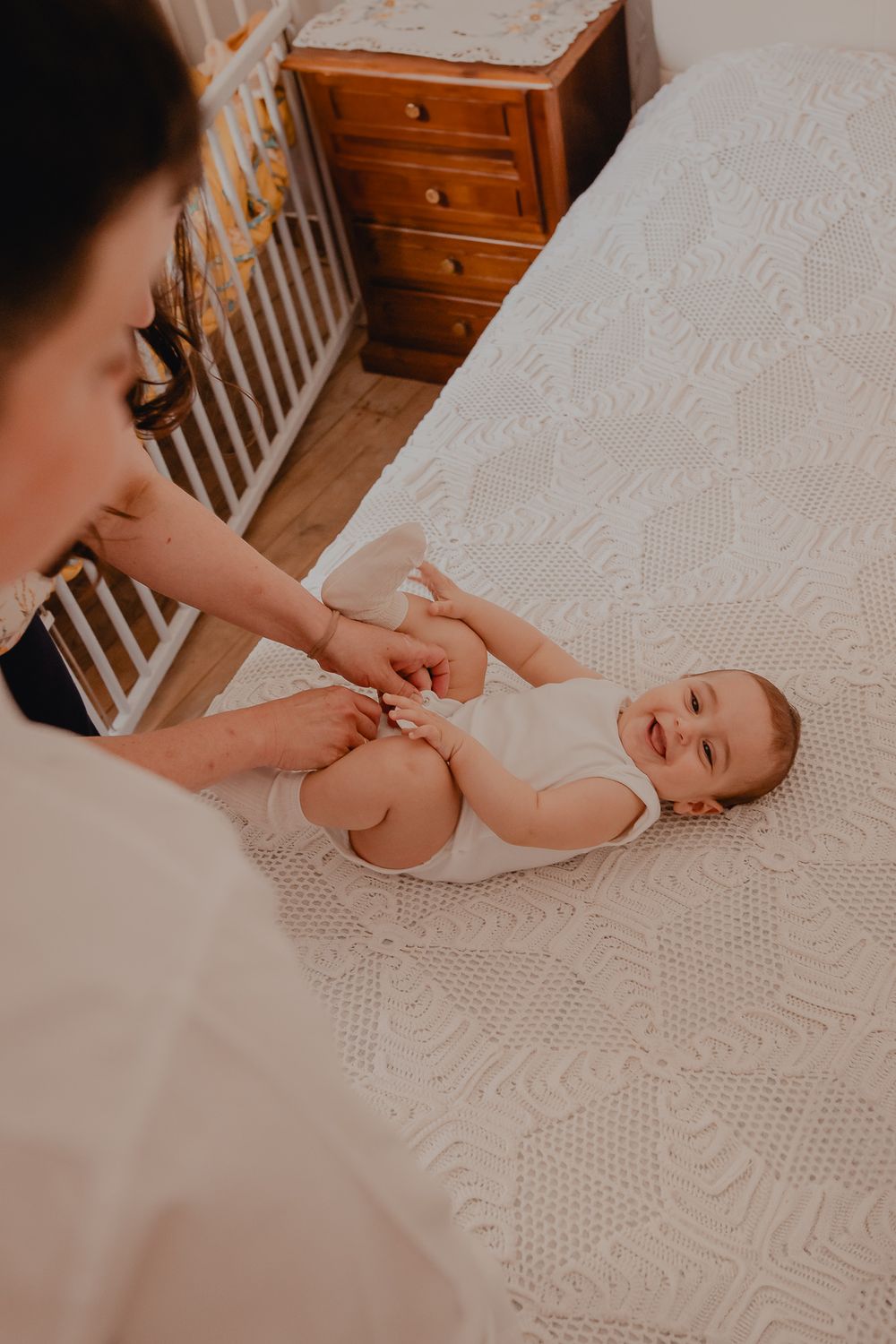 Baby lying on white textured bedding while being dressed.