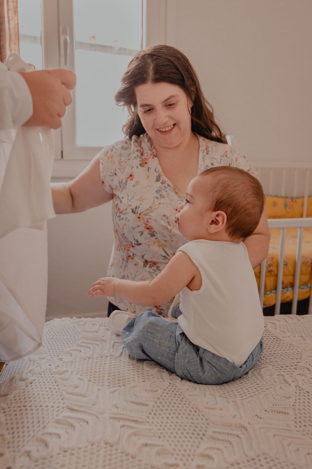 Family sharing joyful moment with baby sitting on textured white bedding.