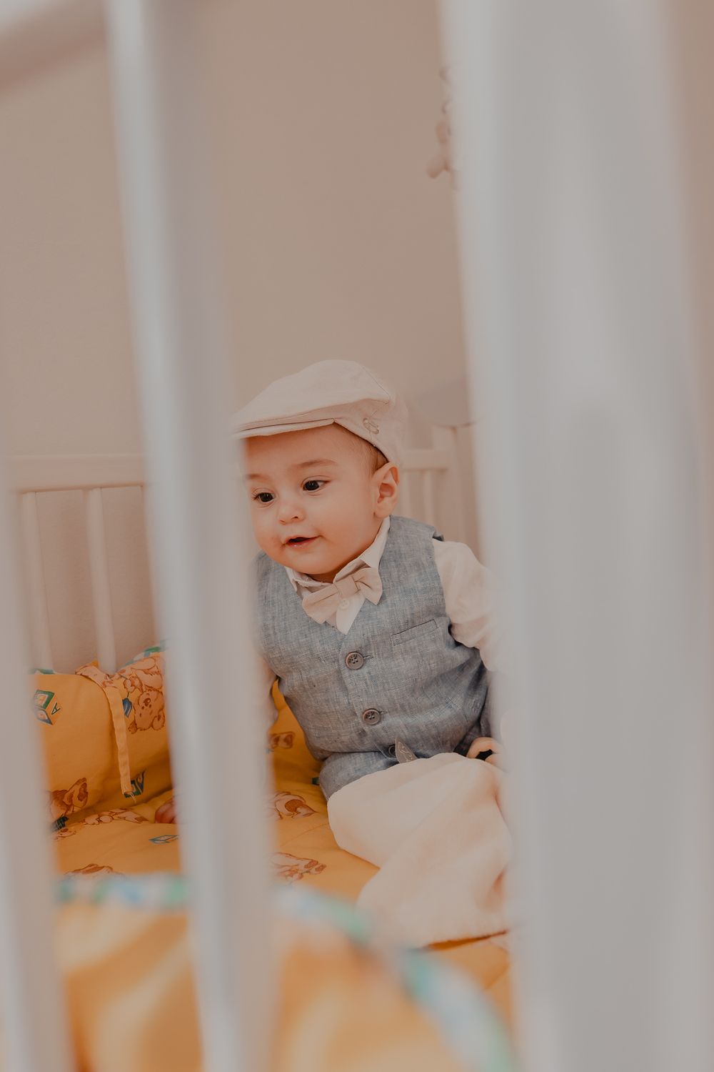 Baby wearing gray outfit smiles while sitting in white crib.