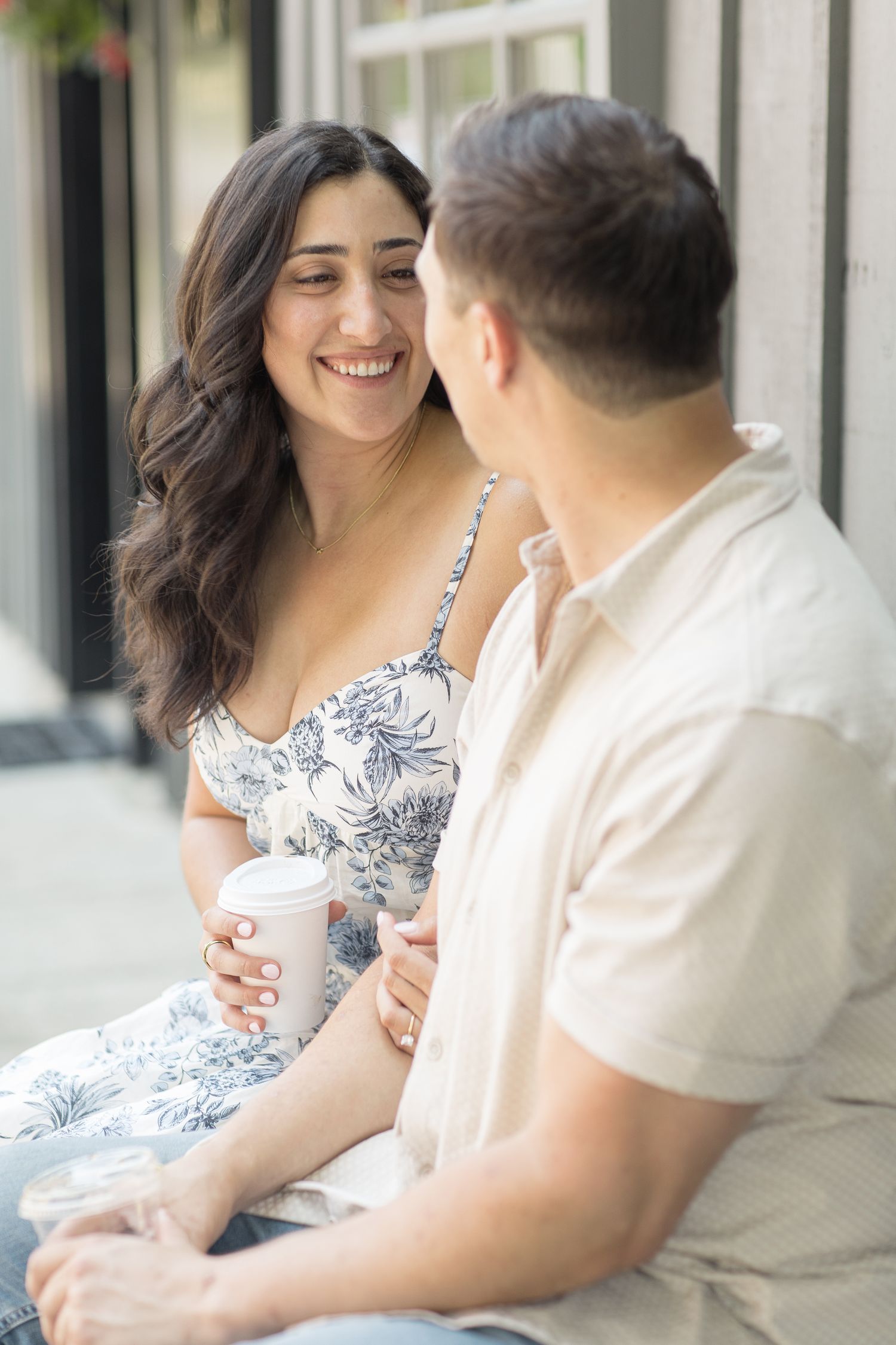 A couple enjoying intimate conversation on a porch while wearing white and floral patterned outfits.
