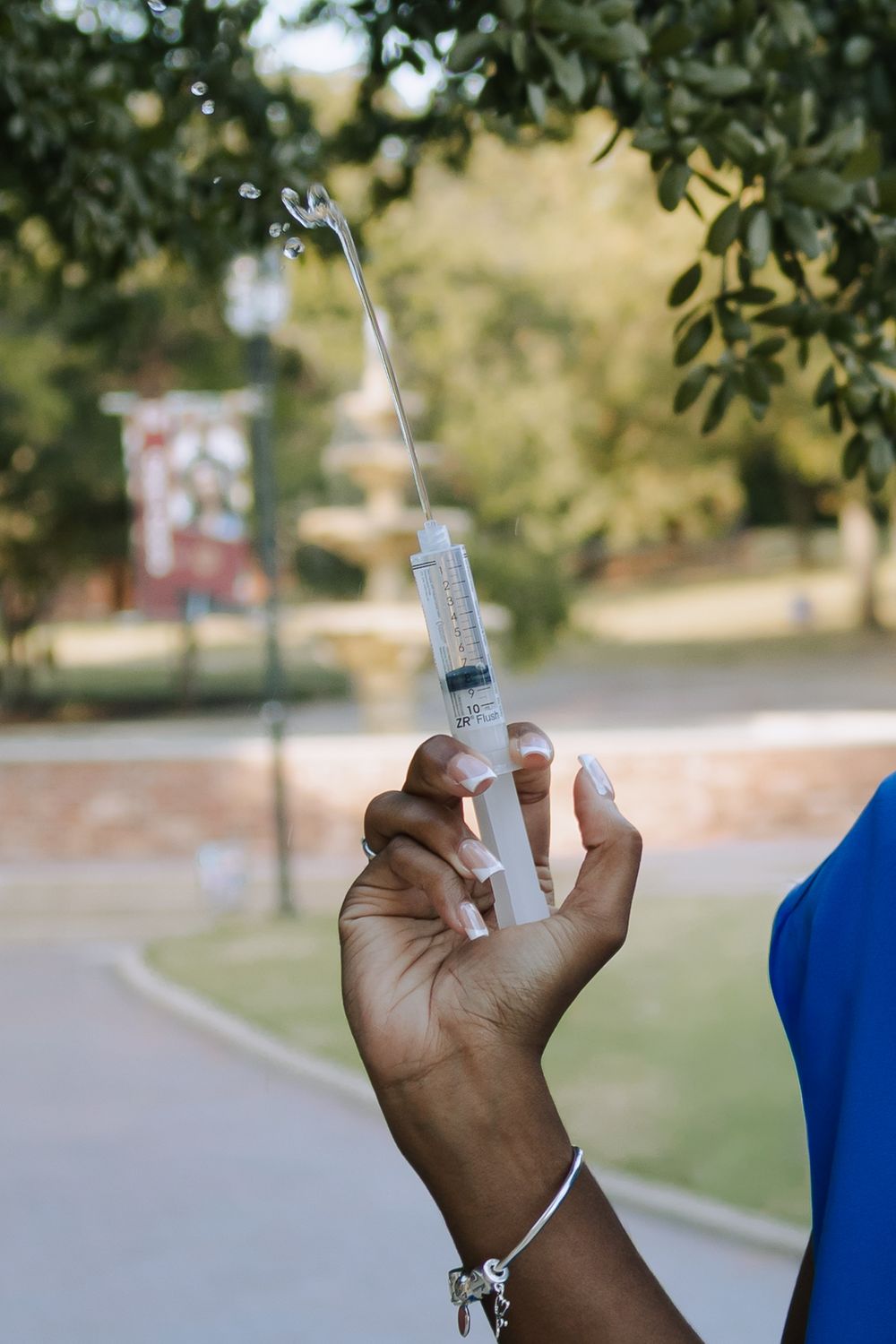 A hand holds a medical syringe with clear liquid against a blurred outdoor background.