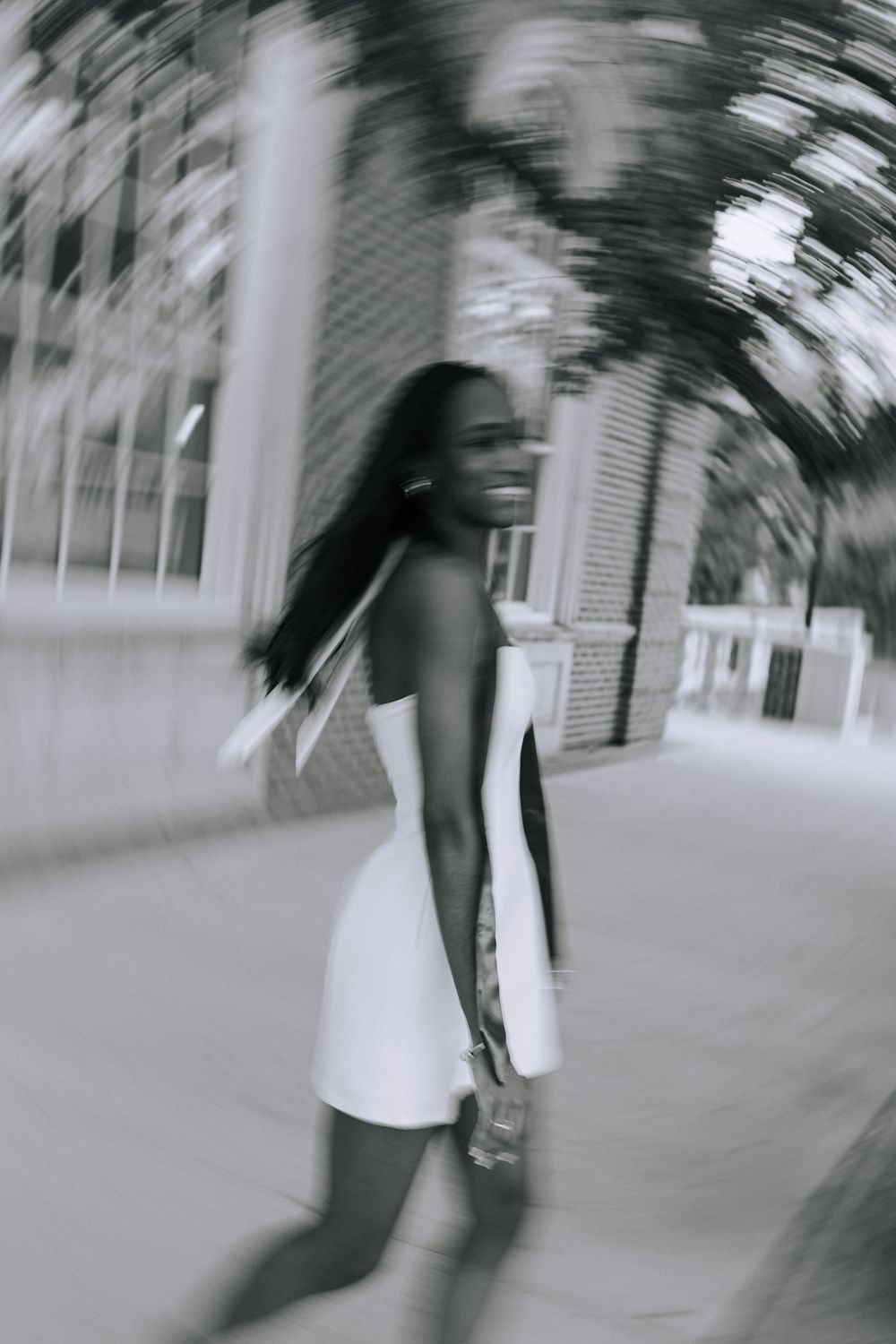 Motion-blurred artistic shot of graduate walking on campus pathway.
