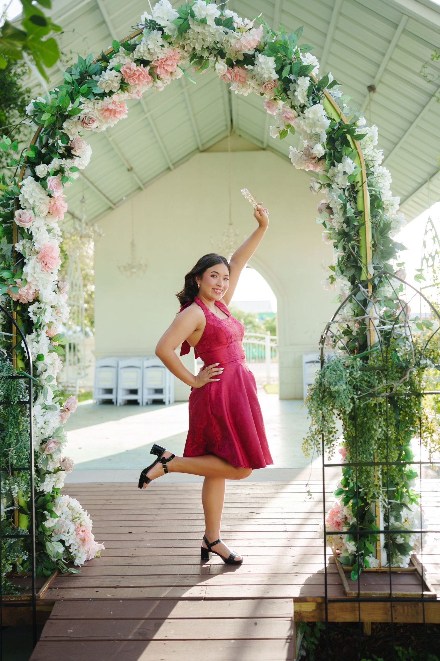 A dancer in a red dress poses gracefully on a white gazebo decorated with pink and white floral garlands.