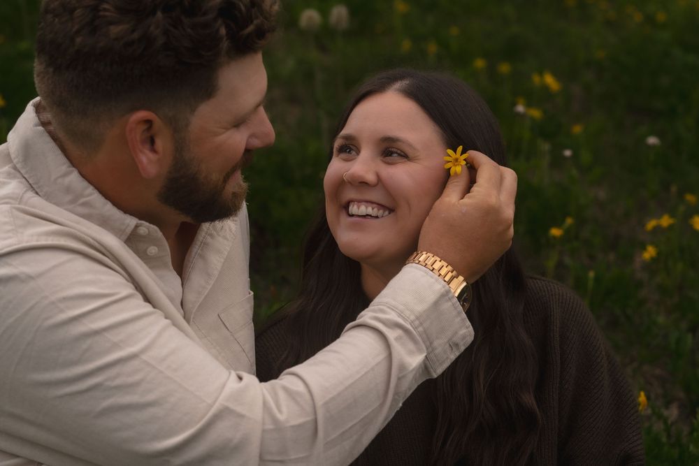 A couple shares a romantic moment while surrounded by wildflowers during an outdoor engagement photo session.