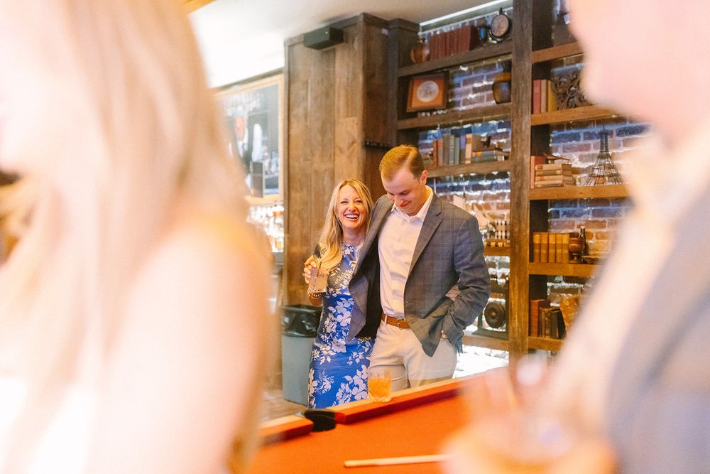 Two people help customers at the wooden front counter of a retail shop with shelving in background.
