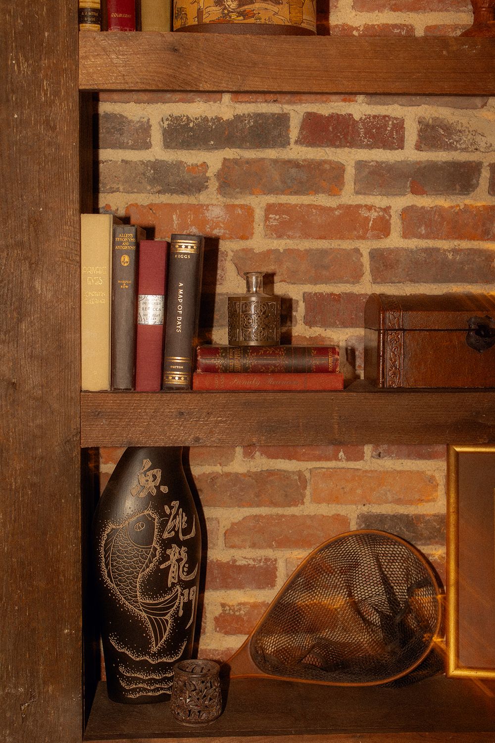 Rustic wooden shelves with antique books and decorative ceramic vessels against an exposed brick wall.
